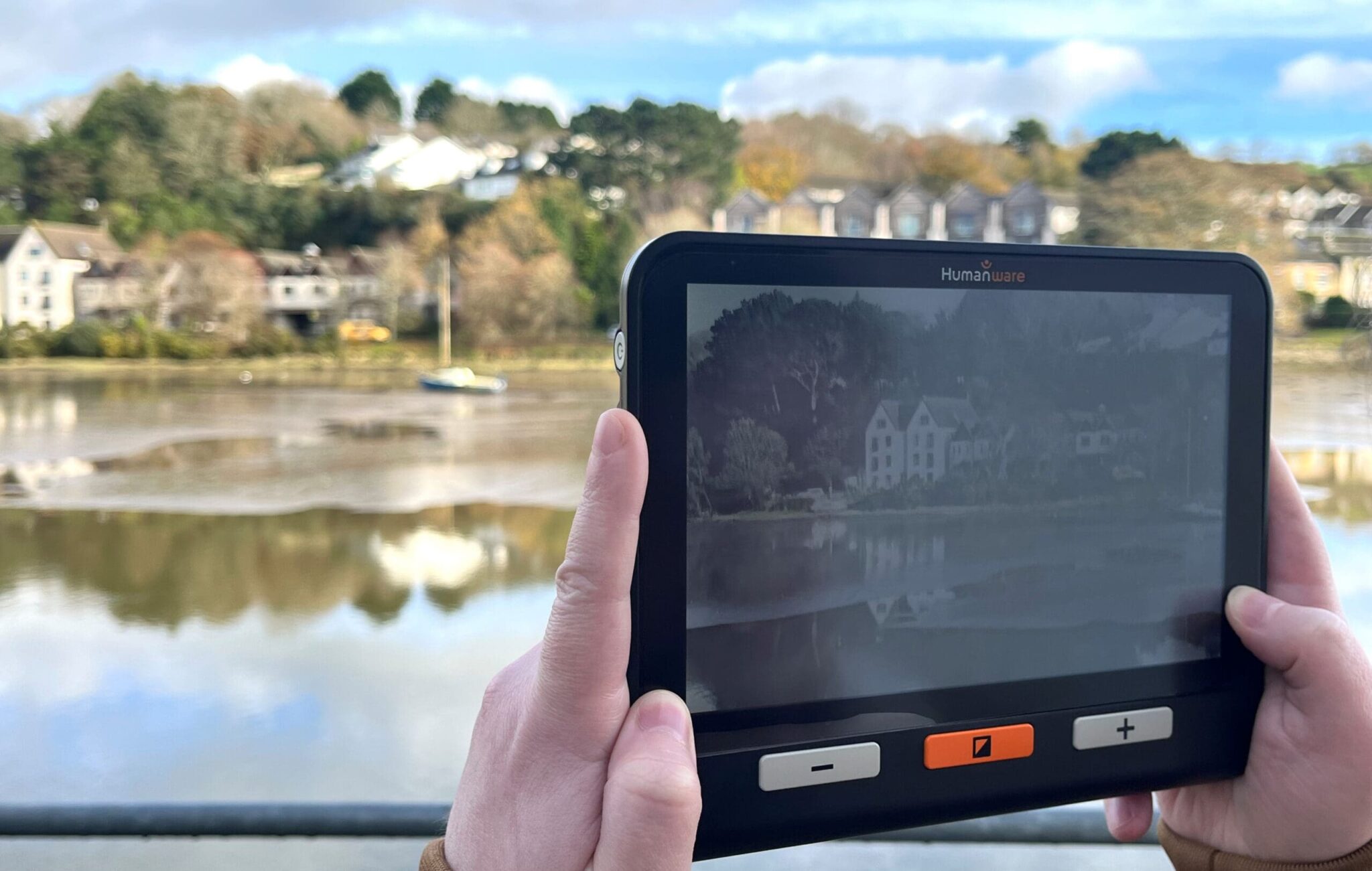 Two hands can be seen on an Assistive Technology magnifier being used to take an image of the surrounding area