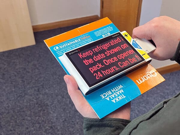 A handheld device with a screen is held over a leaflet, the text from the leaflet is shown on the screen in a much larger font and in a contrasting colour