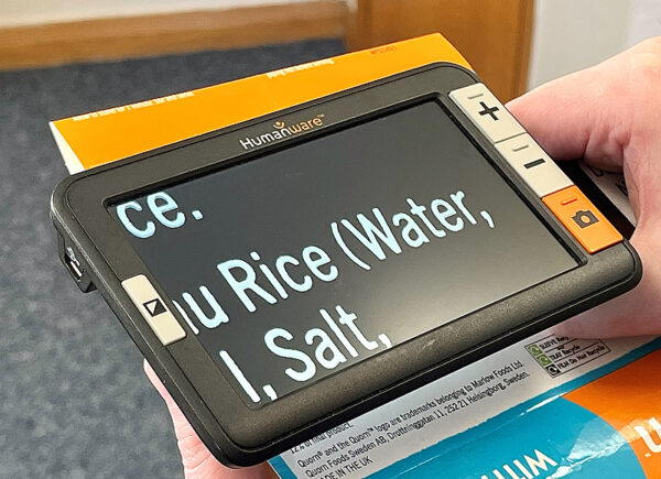 an image showing an electronic magnifier with the Humanware logo on it. It has a screen and four buttons. The buttons have a plus, a minus and an image of a camera. The screen is showing an enlarged version of a recipe. The device shown is the Humanware Explore 5