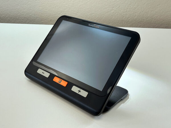 A large rectangular electronic device with a screen and three simple buttons. The device has a built in stand and is shining a light out of the back. The device is the Humanware Explore 8 Electronic Magnifier