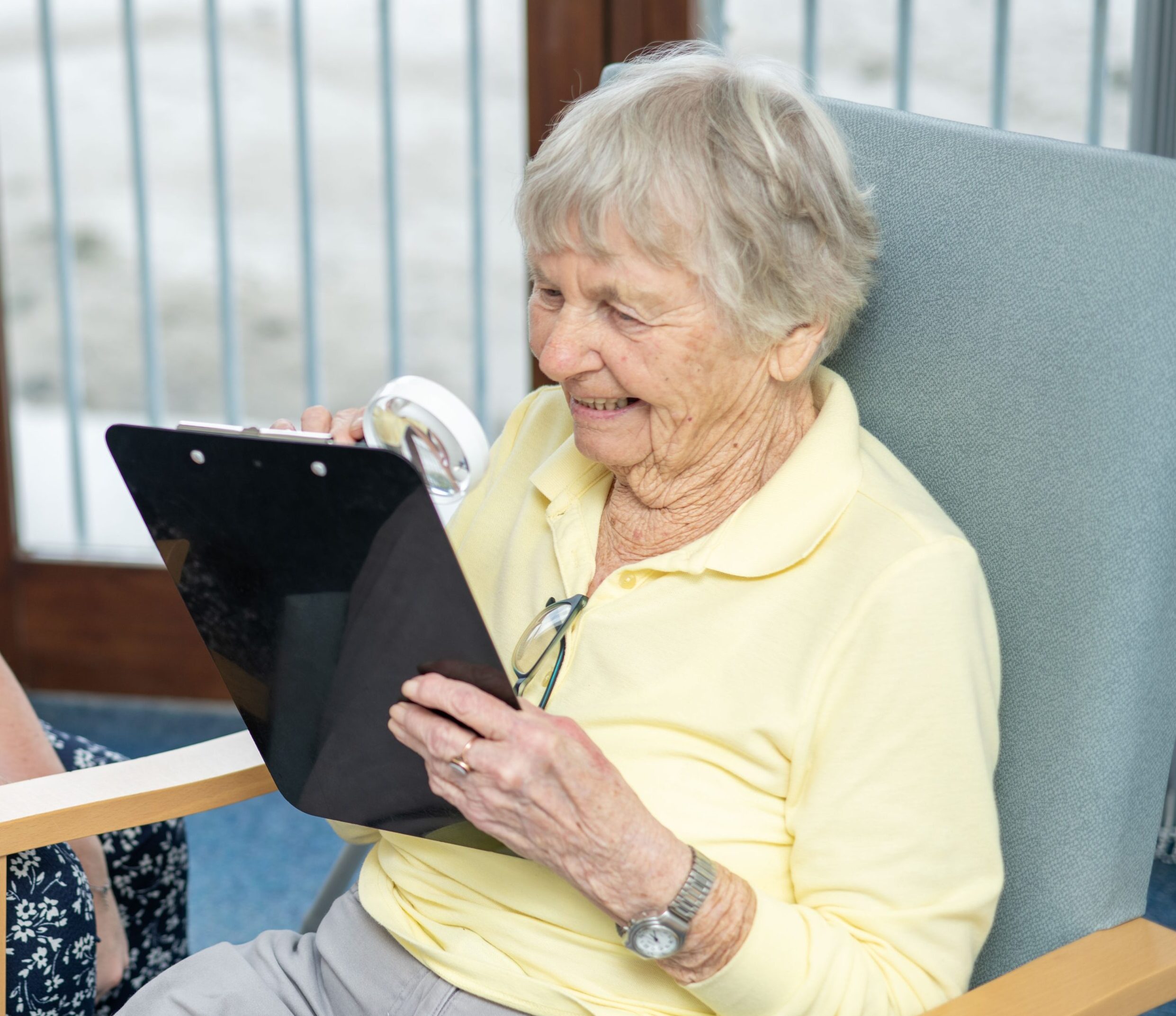 Lady sat in a chair reading a chart with her magnifier.