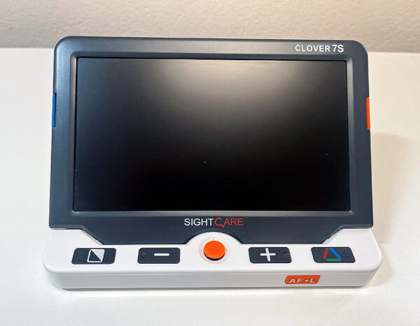 A large rectangular electronic device with a screen and five buttons. The device has a built in stand. The device is the Optima Clover 7S