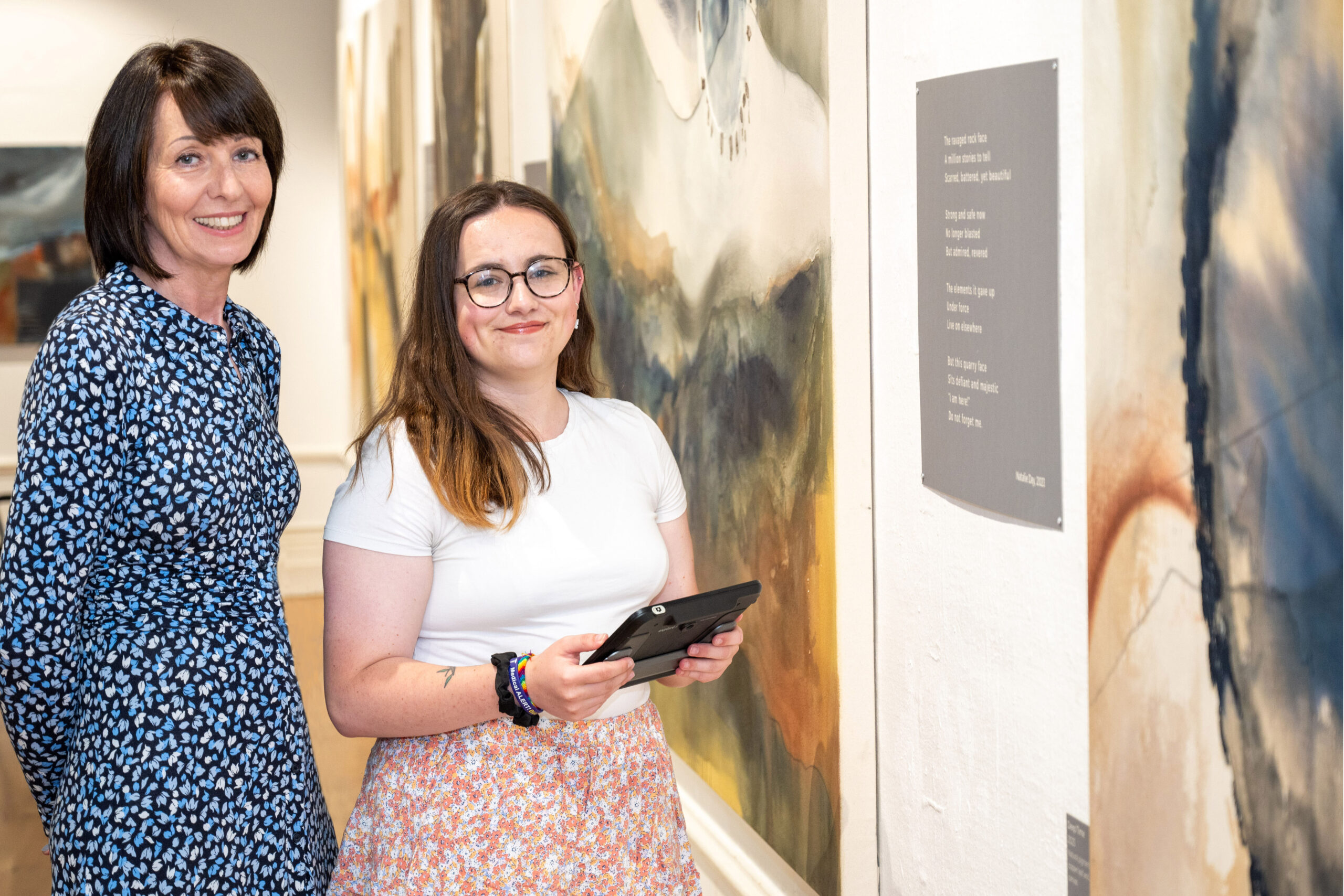 Two ladies standing in an art gallery. The younger lady is holding an electronic magnifier.