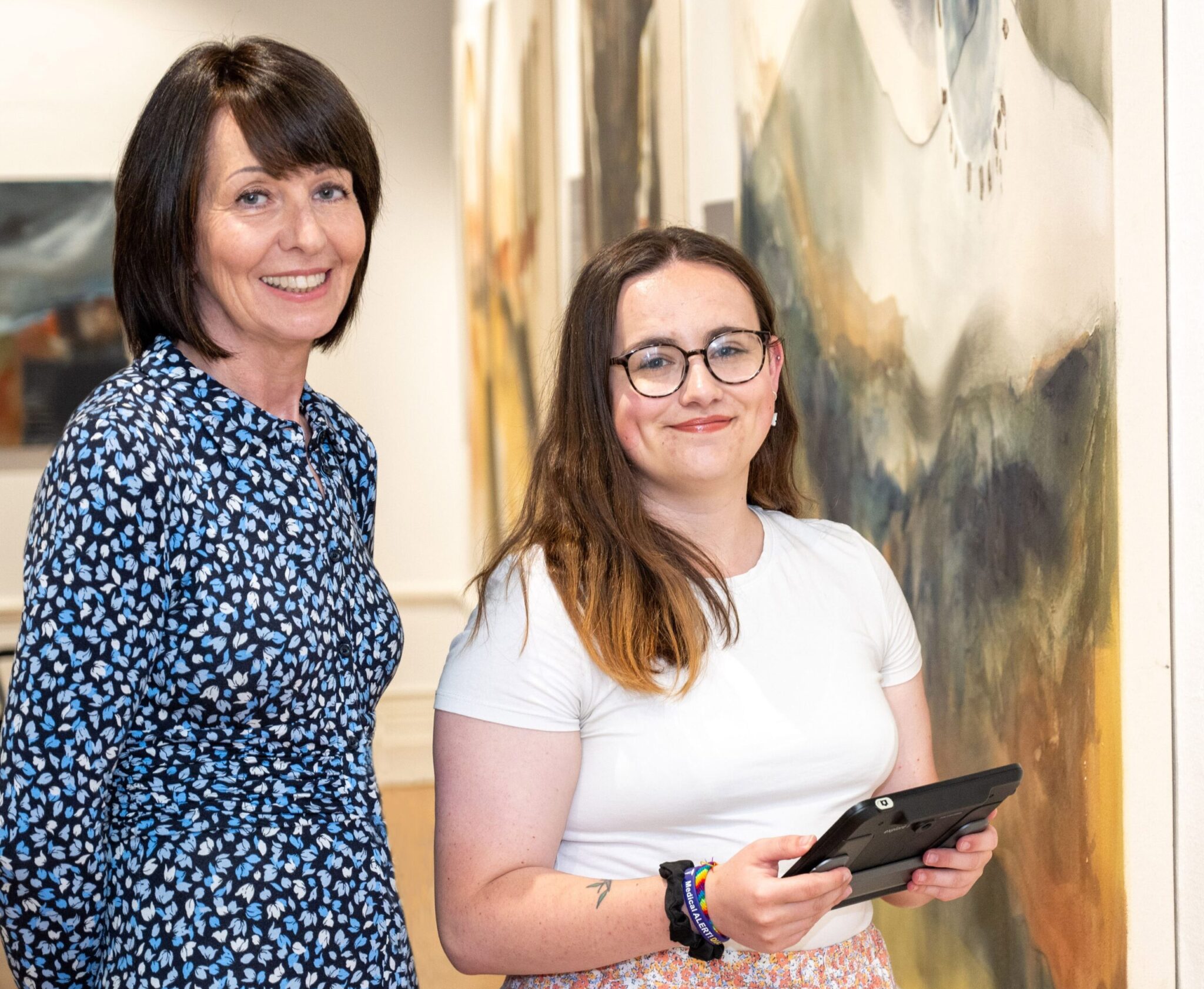 Two ladies standing in an art gallery. The younger lady is holding an electronic magnifier.