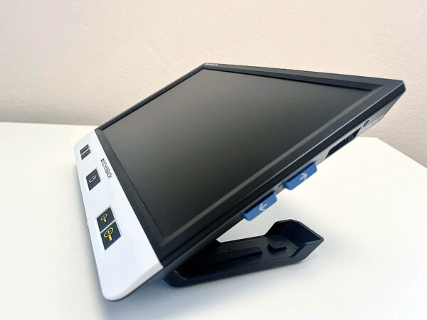 The side view of a large rectangular device with a screen and a stand. It has tactile buttons along the front and side.