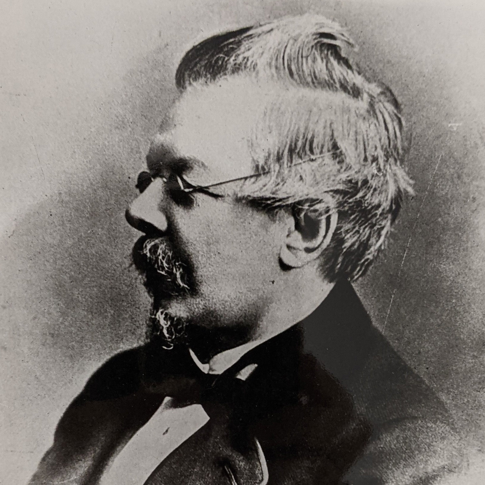 A black and white image of the side profile of a man wearing dark round glasses