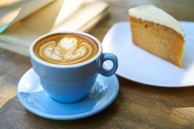 Cup Of Coffee In A Blue Cup Next To Slice Of Cake