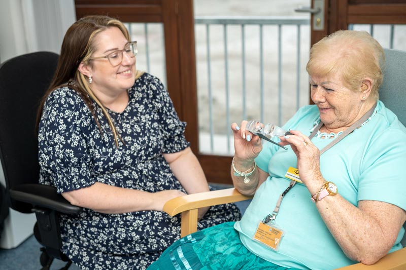 Lady In Flowery Dress Smiling Showing Another Lady Her New Glasses