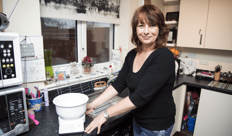 Lady Standing In Kitchen Next To Legacy Gift