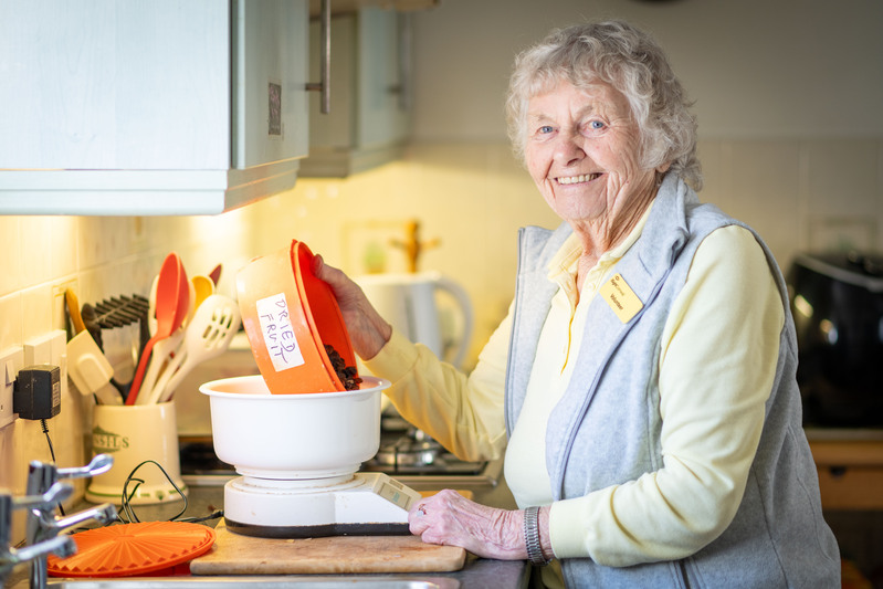 Lady Standing In Kitchen Using Food Scales