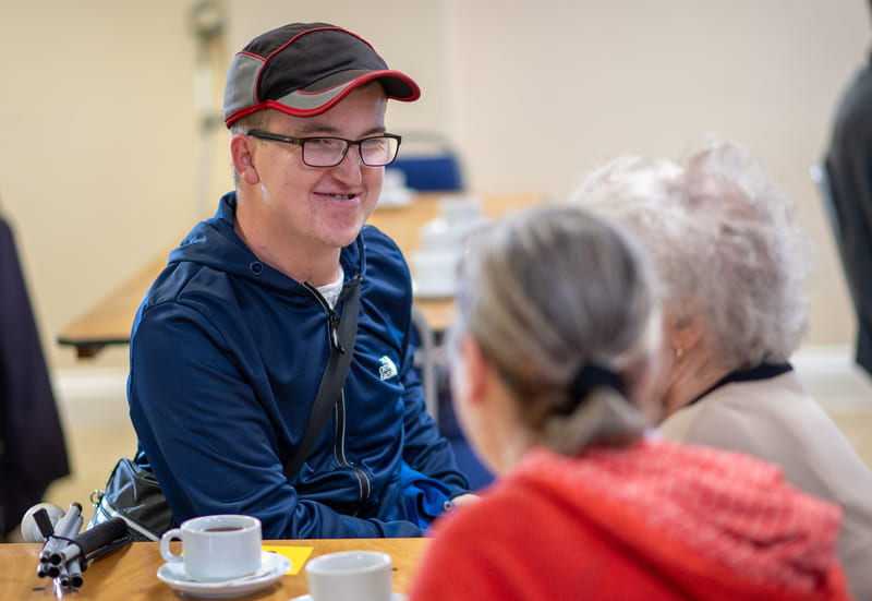 Man In Black Cap And Glasses Talking To Two Women