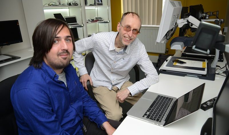 Man In Blue Shirt Sat With Man White Shirt Working On Laptop