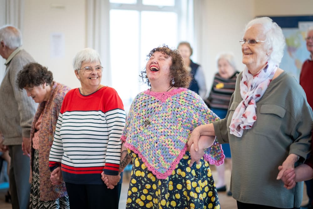 Three Women Standing In A Line Holding Hands And Laughing